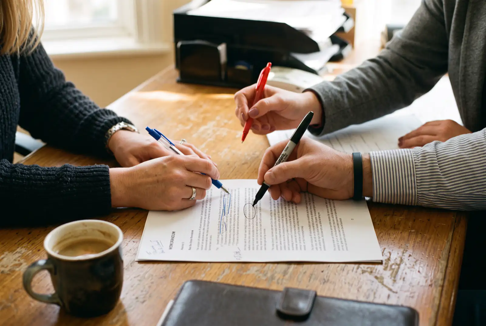 Drei Hände prüfen dasselbe Blatt, jede markiert mit einem anderen Stift eine andere Stelle